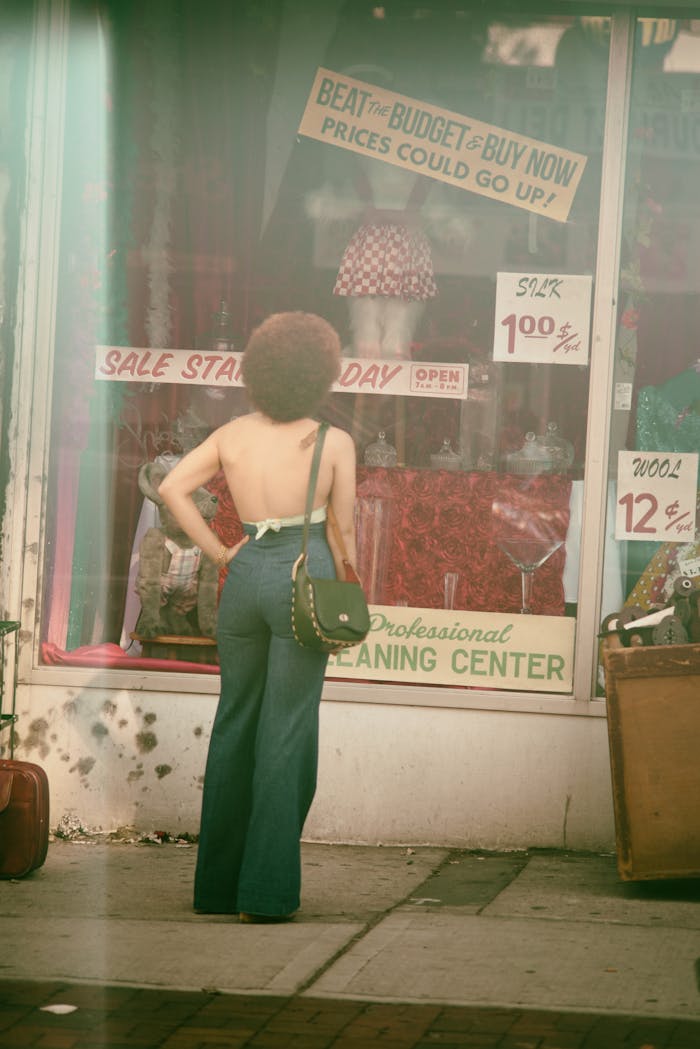 A woman in retro fashion standing outside a vintage store with sale signs in NYC.