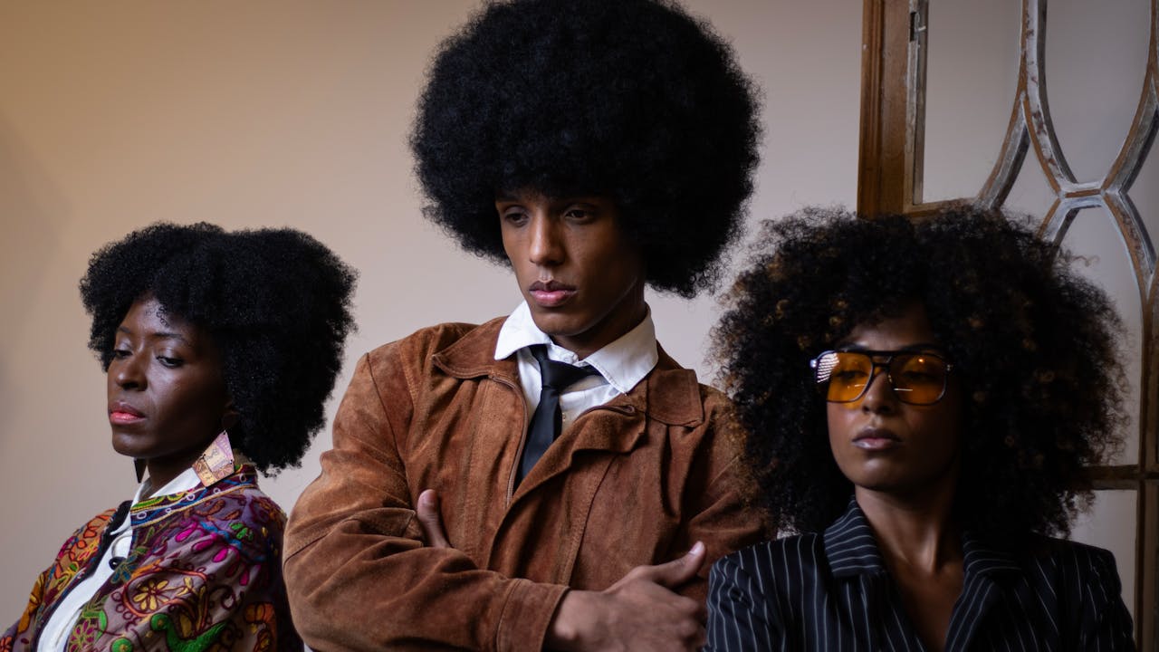 Fashionable trio in vintage attire and afro hairstyles indoors, striking a confident pose.